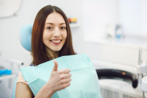 young woman showing thumb up while sitting in medical chair at dental clinic stock picture