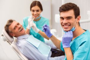 Young dentist and his assistant treating elderly man stock image